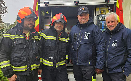 Vier Männer in Feuerwehruniform vor einem Einsatzfahrzeug.