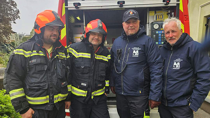 Vier Männer in Feuerwehruniform vor einem Einsatzfahrzeug.