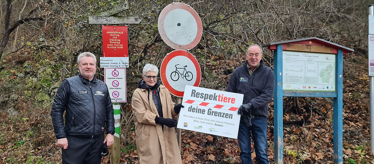 Drei Personen mit dem Schild der Aktion am Eingang des Stadtwaldes.