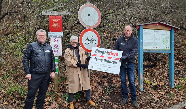 Drei Personen mit dem Schild der Aktion am Eingang des Stadtwaldes.