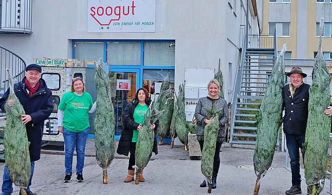 Eine Gruppe von Menschen steht mit verpackten Christbäumen vor dem Soogut-Markt in Mödling.