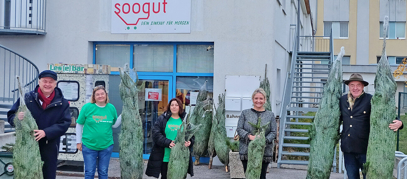 Eine Gruppe von Menschen steht mit verpackten Christbäumen vor dem Soogut-Markt in Mödling.