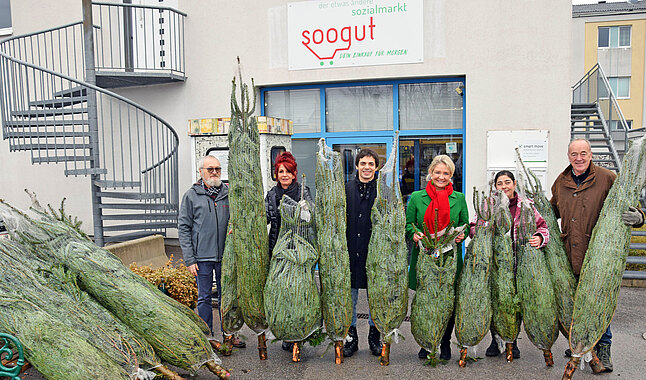 Eine Gruppe von Personen mit Christbäumen vor einem Sozialmarkt.