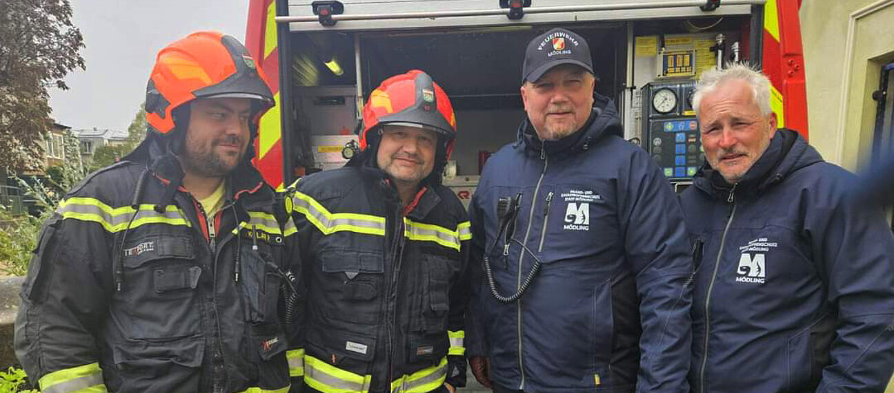 Vier Männer in Feuerwehruniform vor einem Einsatzfahrzeug.