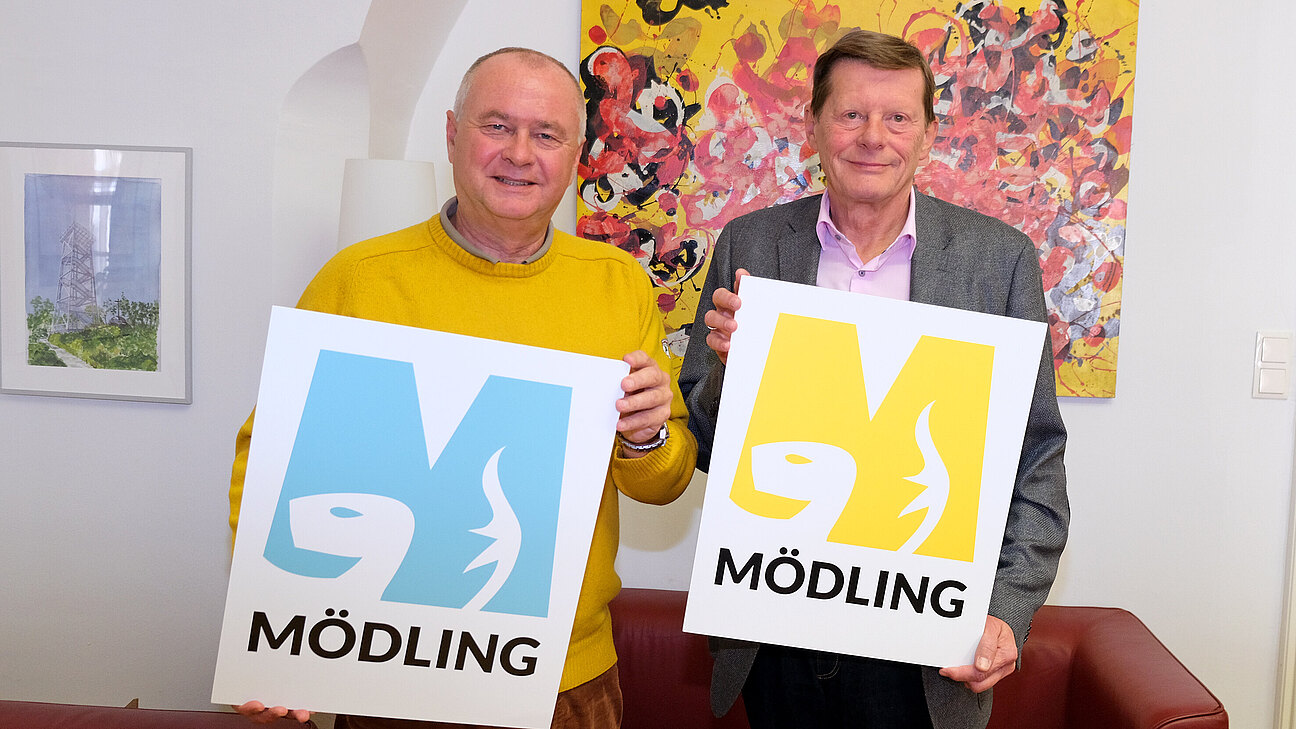 Zwei Männer halten große Mödling Ms auf Tafeln.